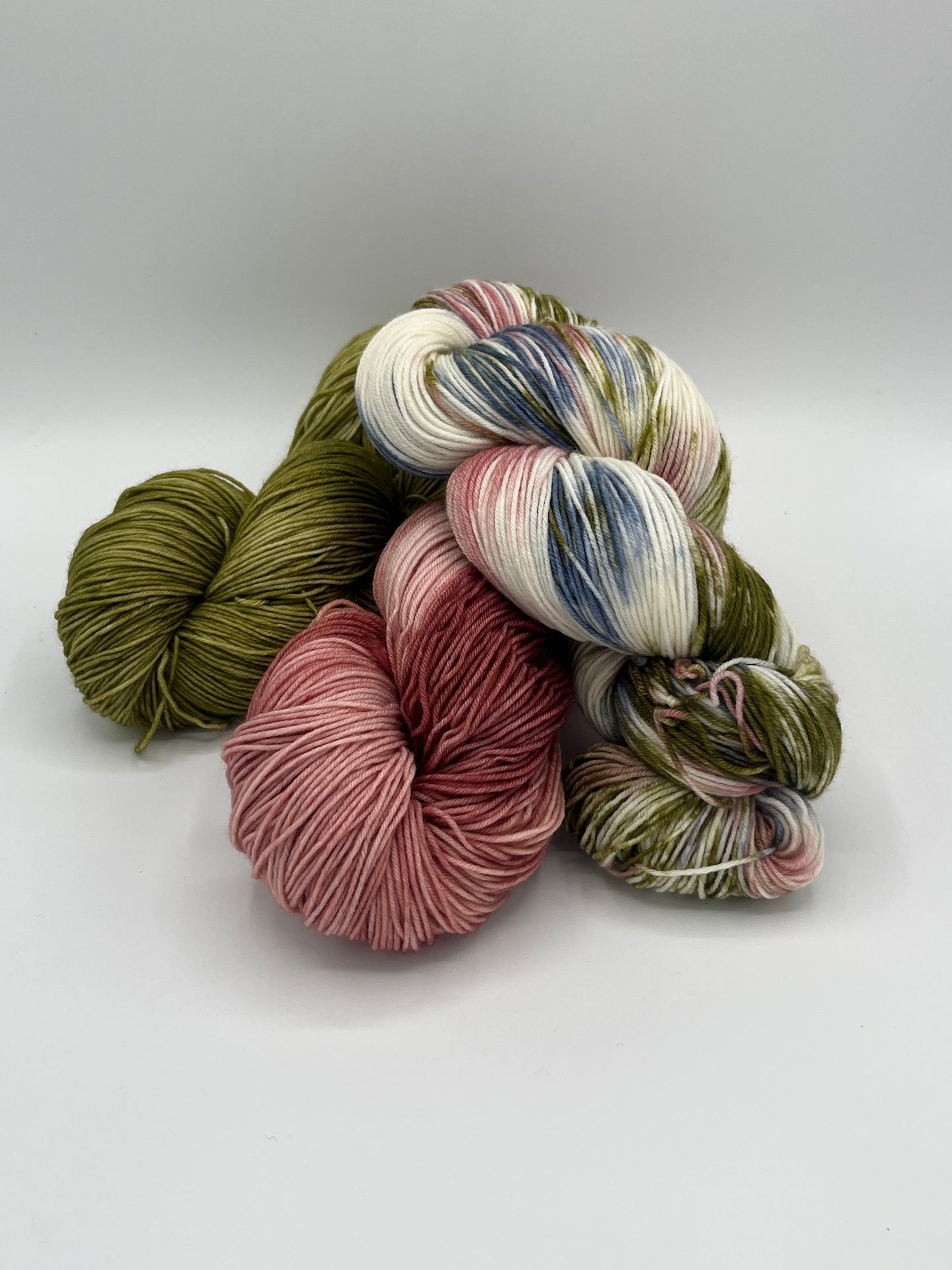 Drei Stränge Sockenwolle, farblich und thematisch aufeinander abgestimmt, in den Farben Rosenprinzessin (Altrosatöne), Moosmagie (dunkle und mittlere Grüntöne) und Königskinder im Wald (Natur, Altrosa, Grün und Blau)