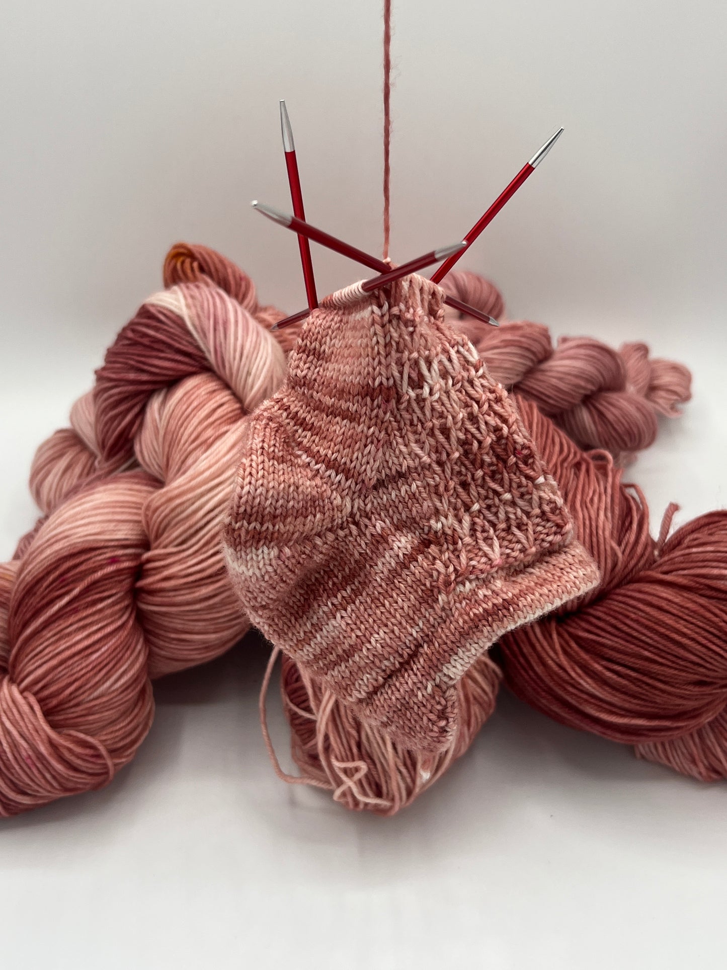 Eine begonnene Sneakersocke Luftikus in der Farbe Rosenprinzessin mit dem entsprechenden Strang im Hintergrund, Altrosatöne